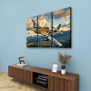 A three-panel canvas wall art set depicting a vintage military airplane flying over mountains under a dramatic cloudy sky, displayed above a wooden console table in a styled room.