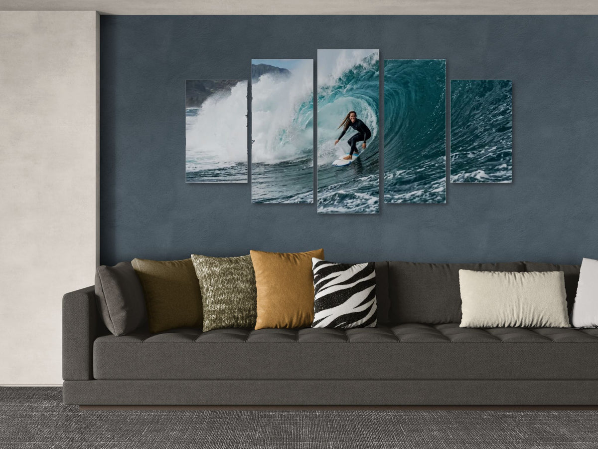Five-panel wall art of a surfer on a wave above a gray sofa with patterned cushions.