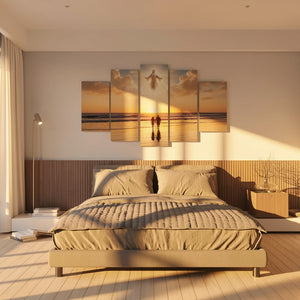 A 5-panel canvas wall art set depicting a sunset beach scene with a figure walking on the sand, displayed above a bed in a modern, warm-toned bedroom.