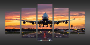 A five-panel canvas wall art set depicting a large commercial airplane on a runway at sunset, shown against a dark gray background.