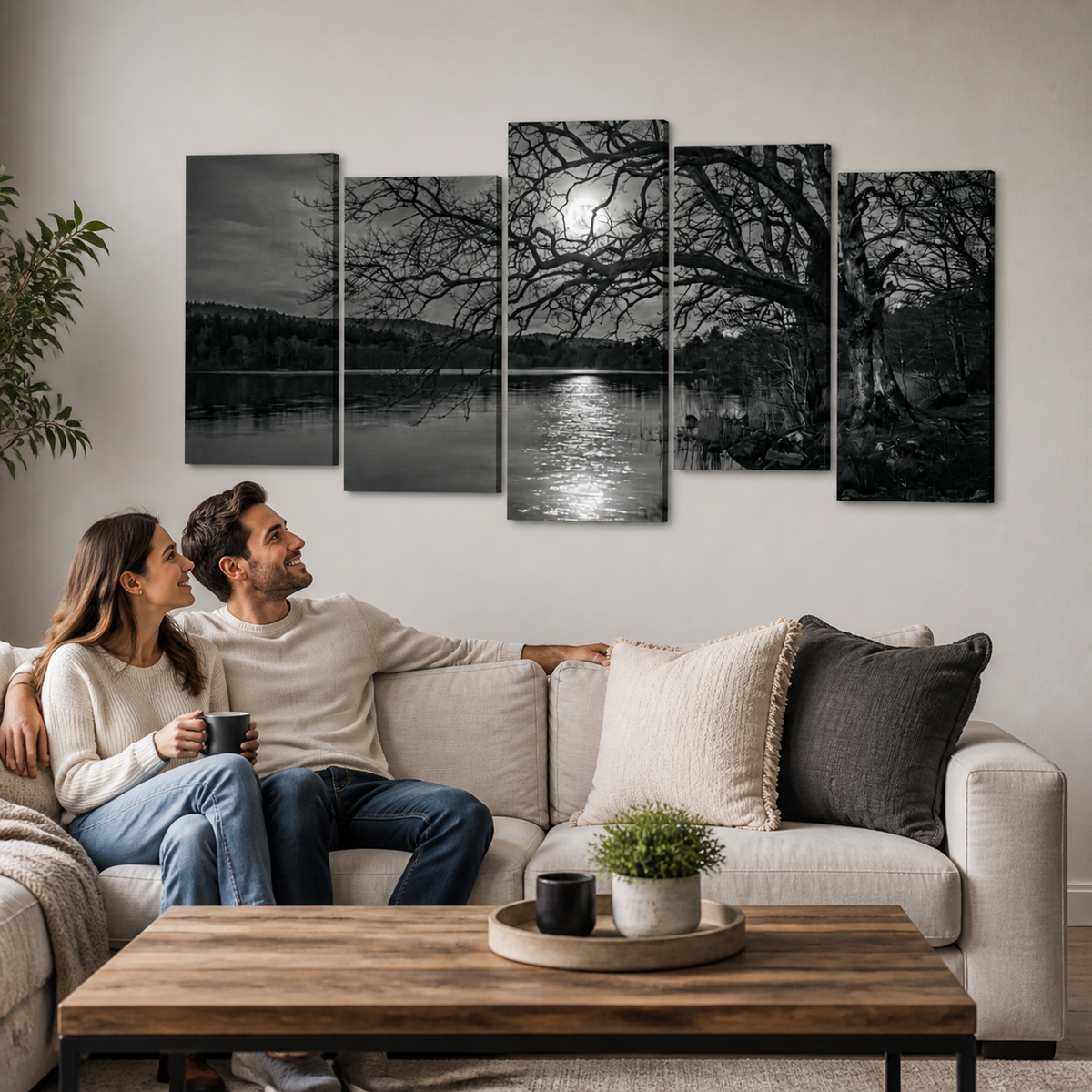 A five-panel black and white canvas wall art set depicting a moonlit lake scene with bare trees, shown hanging above a couple sitting on a light beige sofa in a modern living room.