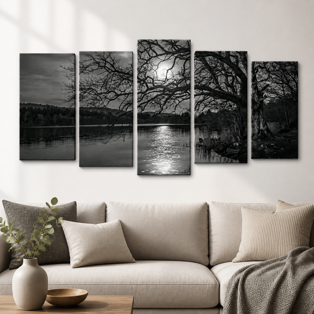 A five-panel black and white canvas wall art set depicting a moody lakeside forest scene with bare trees and moonlit reflections, displayed above a beige sofa in a modern living room.
