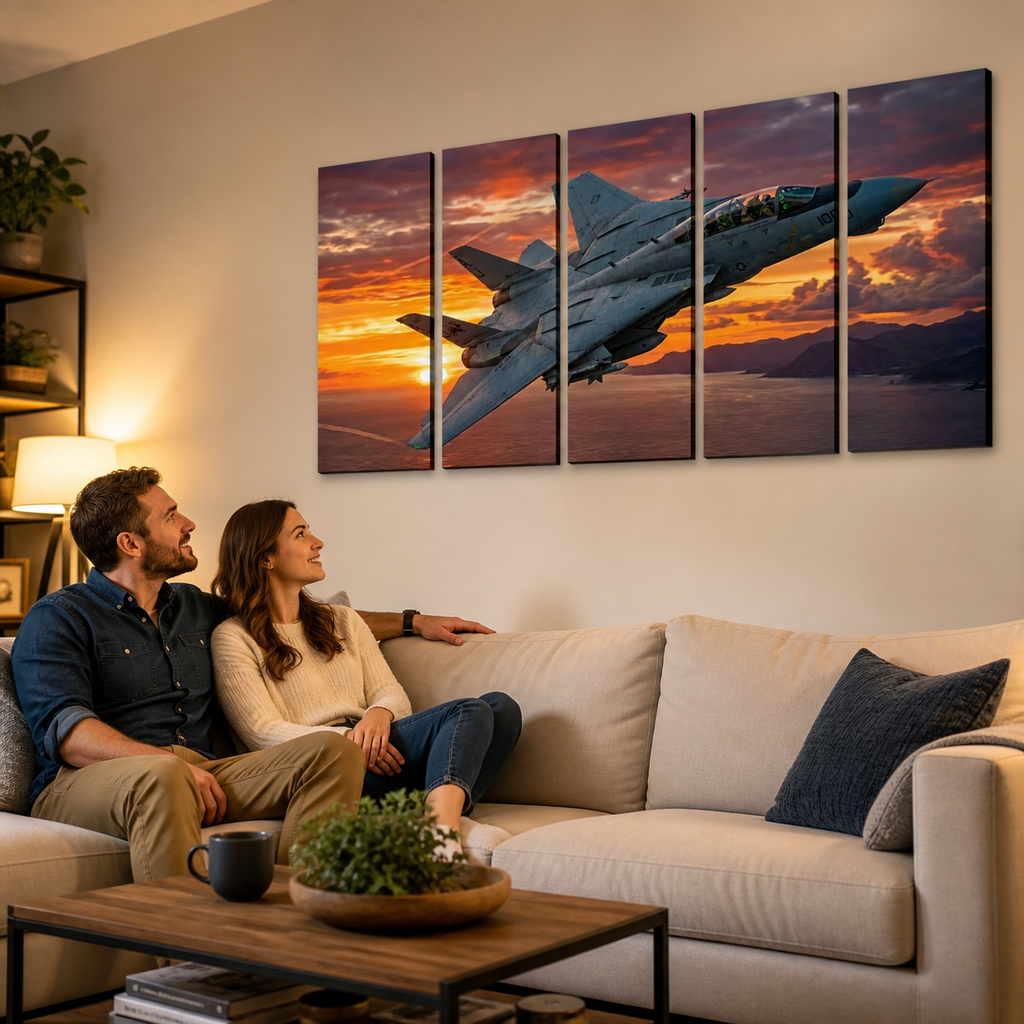 A couple sits on a beige sofa in a living room, looking at a five-panel canvas wall art print depicting a gray Grumman F-14 military fighter jet flying against a dramatic orange and pink sunset sky.