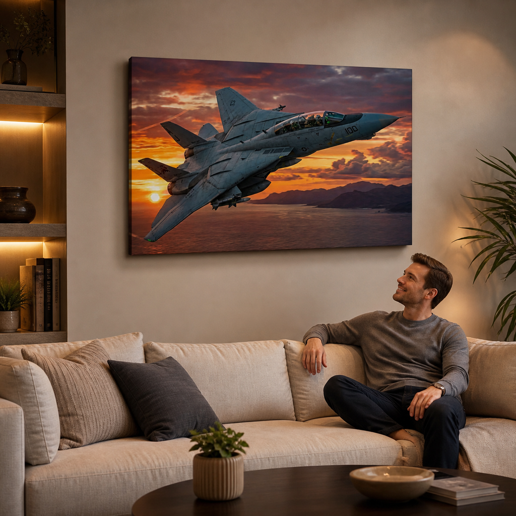 A large rectangular wall art print showing a gray Grumman F-14 Tomcat  military fighter jet flying over a sunset over water, displayed above a beige sofa in a modern living room with a seated man looking at the artwork.