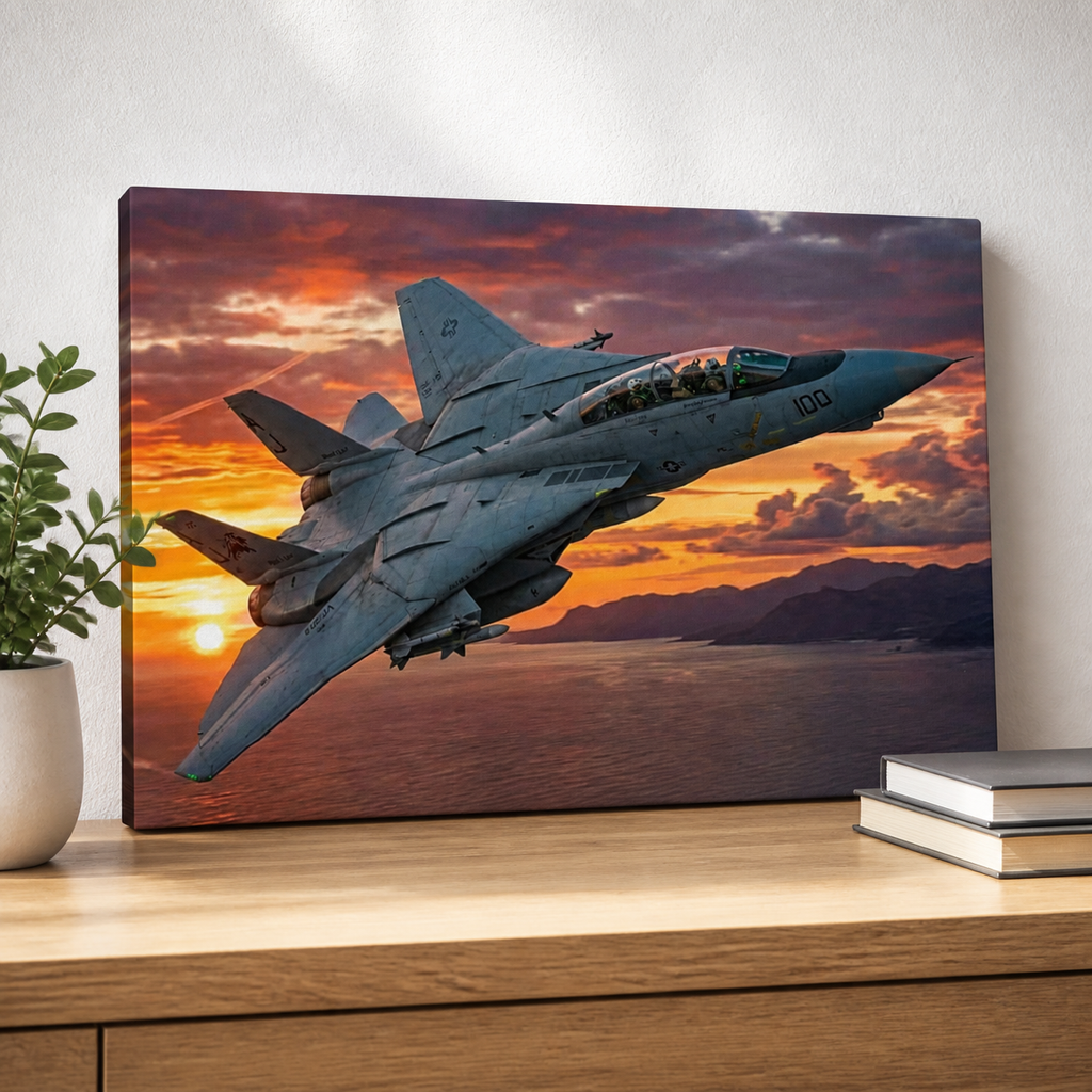 A rectangular wall art print or canvas showing a gray Grumman F-14 Tomcat  fighter jet flying over water at sunset, displayed on a wooden surface against a light wall with a plant and books nearby.