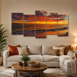 A 5-panel canvas wall art set depicting a dramatic orange and red Indian Rocks,  FL sunset over the ocean, displayed on a beige wall above a modern beige sectional sofa in a living room setting.