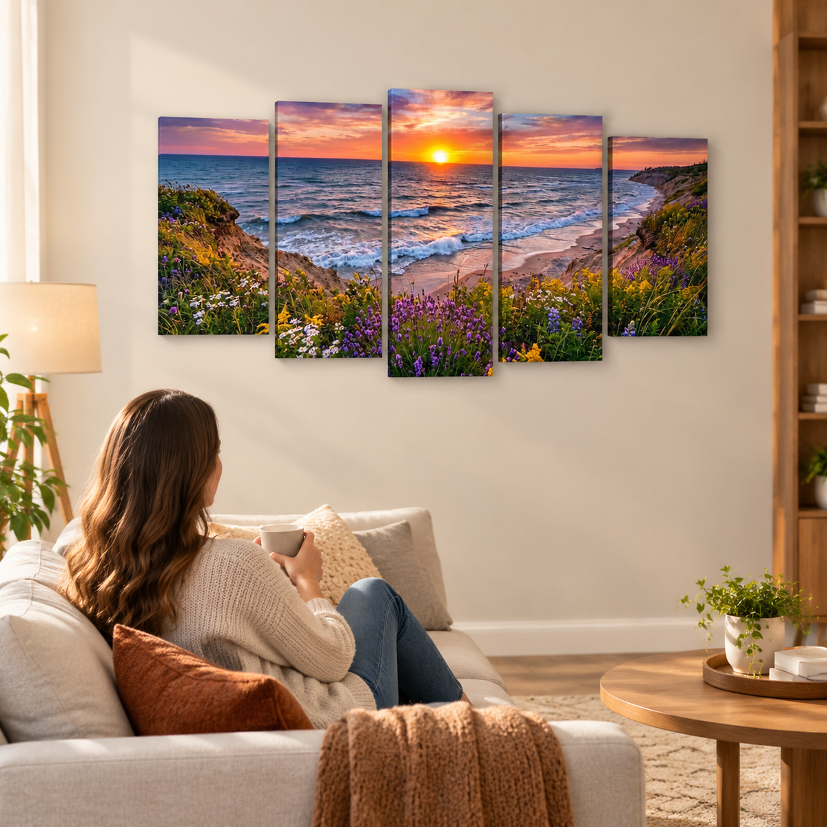 A five-panel canvas wall art set depicting a colorful sunset over a beach and ocean, shown hanging on a wall in a modern living room setting with a woman sitting on a sofa.