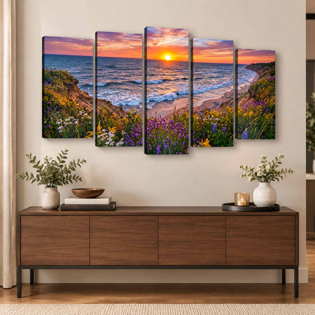 A five-panel canvas wall art set depicting a coastal sunset with ocean waves, sandy beach, and wildflowers in the foreground, displayed above a wooden console table in a styled living room.