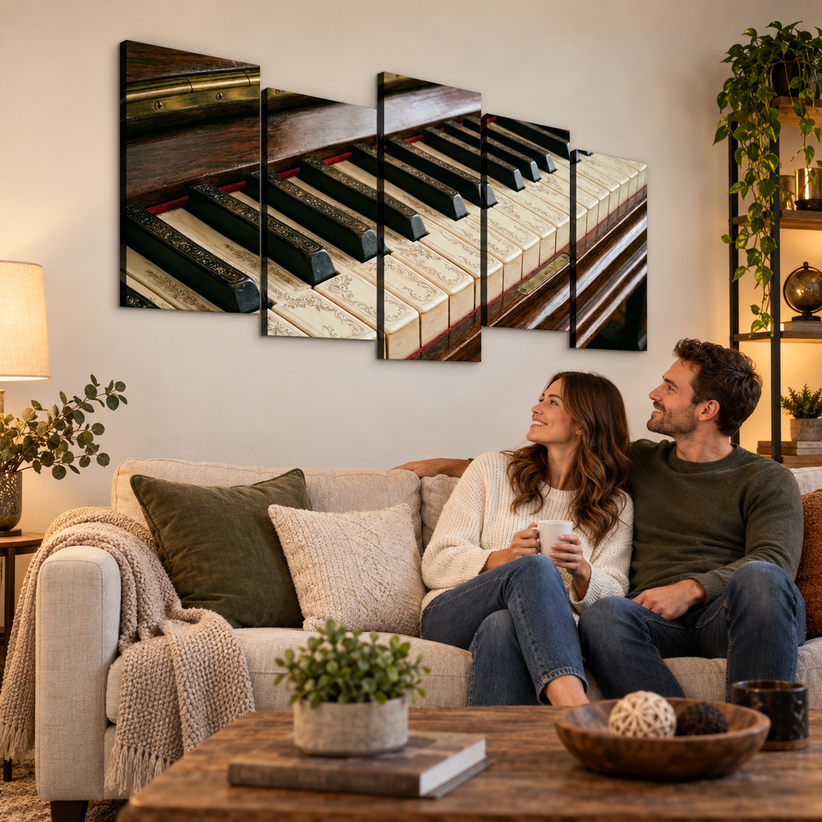 A couple sits on a beige sofa in a cozy living room, looking at a multi-panel canvas wall art print depicting a close-up of piano keys. The room is styled with a wooden coffee table, plants, and warm ambient lighting.