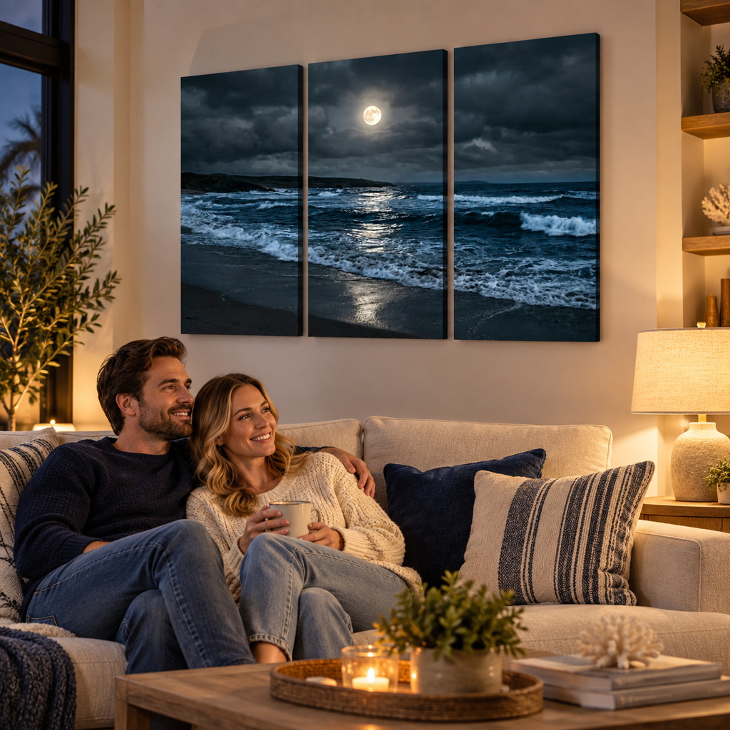 A three-panel canvas wall art set depicting a dramatic moonlit ocean scene, displayed above a couple sitting on a beige sofa in a warmly lit living room.