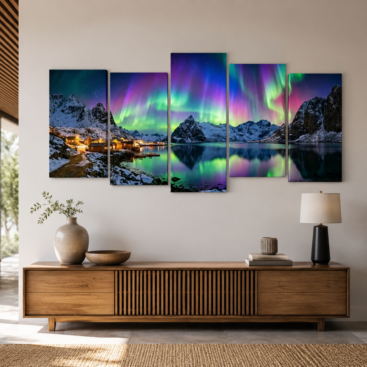 A five-panel canvas wall art set depicting a snowy mountain landscape with glowing northern lights reflected in a calm lake, displayed above a wooden console table in a modern living room setting.
