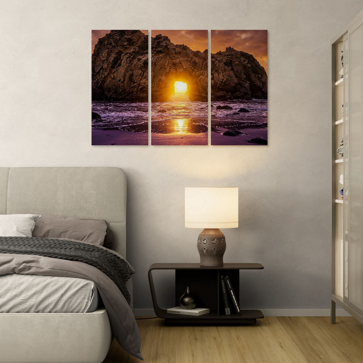 Triptych wall art of a sunset over water in a bedroom setting with a lamp and books on a nightstand.