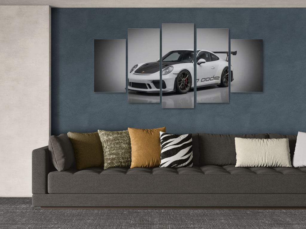 Wall art of a white porsche 911 gt3 991.2 generation sports car on a dark blue wall above a gray sofa with patterned cushions.