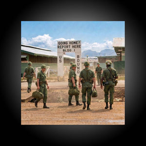 Group of soldiers walking towards a sign indicating they are bound for a location, with mountains in the background.