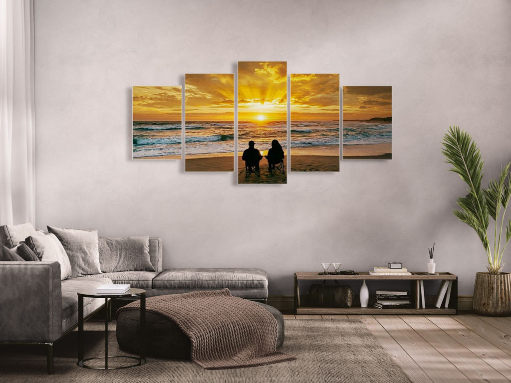 Five-panel wall art of a sunset over the ocean with people on a beach, displayed in a living room.