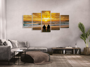 Five-panel wall art of a sunset over the ocean with people on a beach, displayed in a living room.