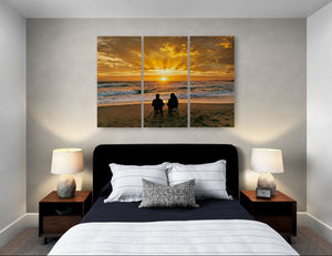 Bedroom with a large wall art of a sunset over the ocean and two people sitting on the beach.
