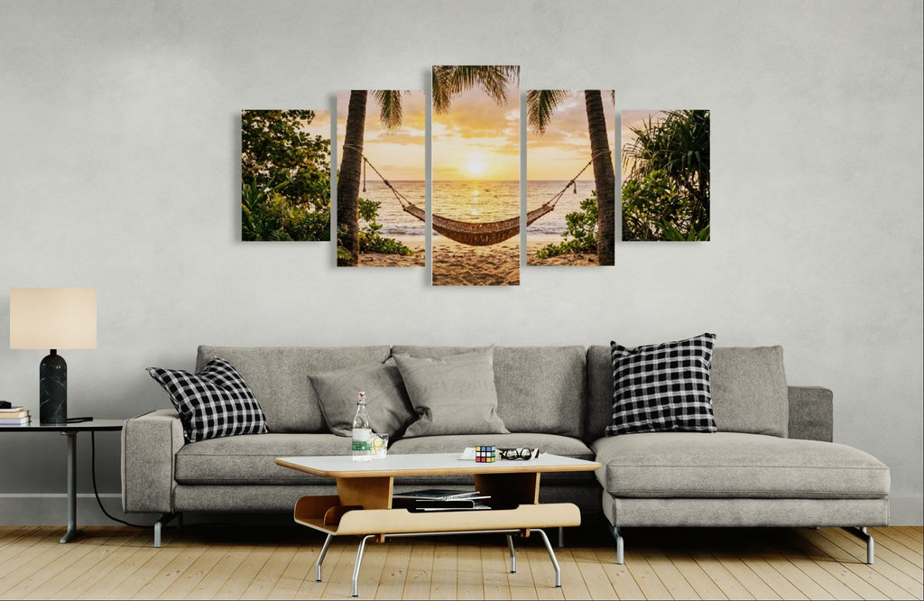 Gray sectional sofa with decorative pillows in a living room setting, featuring a wall art piece of a sunset over a hammock between palm trees.