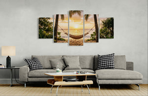 Gray sectional sofa with decorative pillows in a living room setting, featuring a wall art piece of a sunset over a hammock between palm trees.
